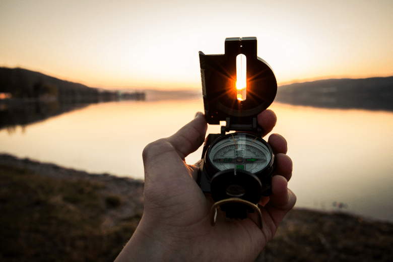 A person holding up a compass towards the sun during sunset
