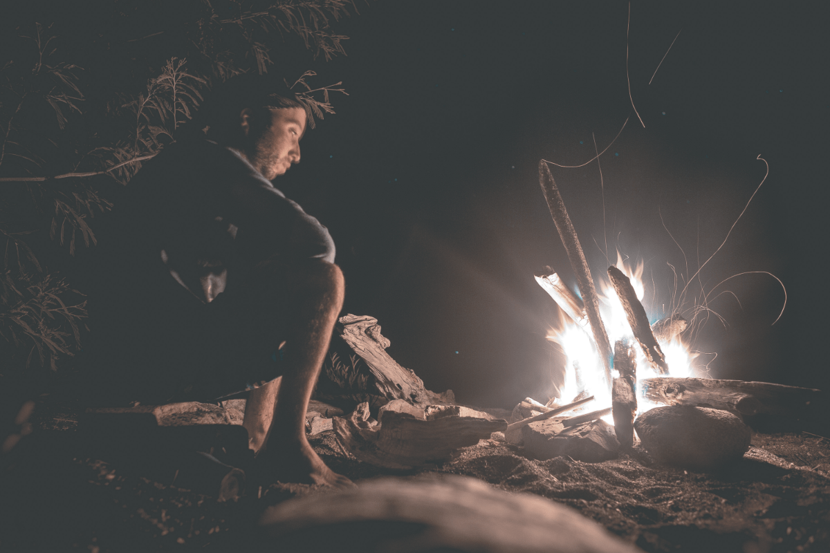 man looking mesmerized by campfire during the night